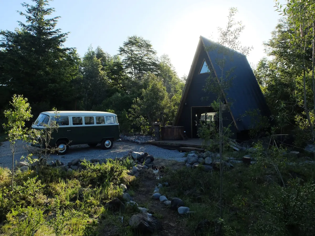 La cabaña tipo A entre el bosque en un día soleado, con una furgoneta clásica al lado