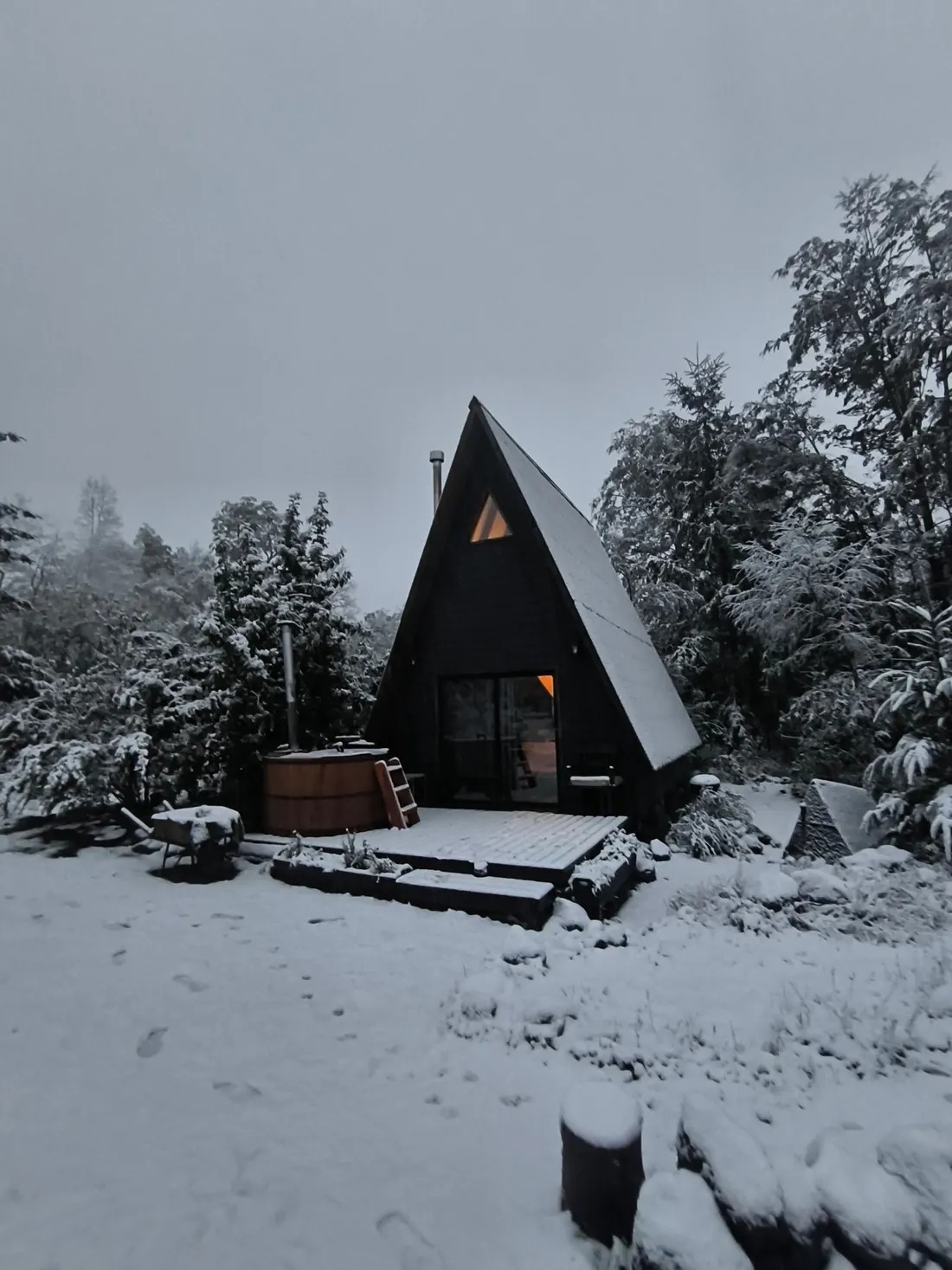 The A-frame cabin covered in snow at dusk, with its windows lit