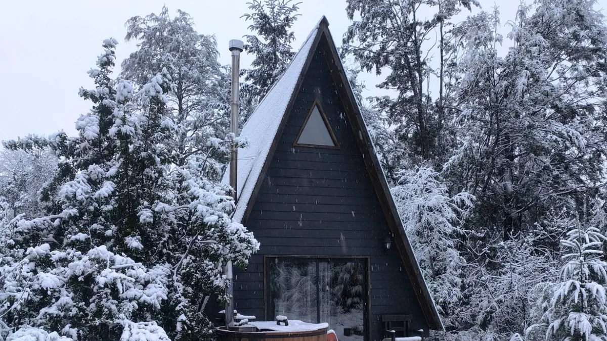 La cabaña tipo A cubierta de nieve, con la tinaja en la terraza